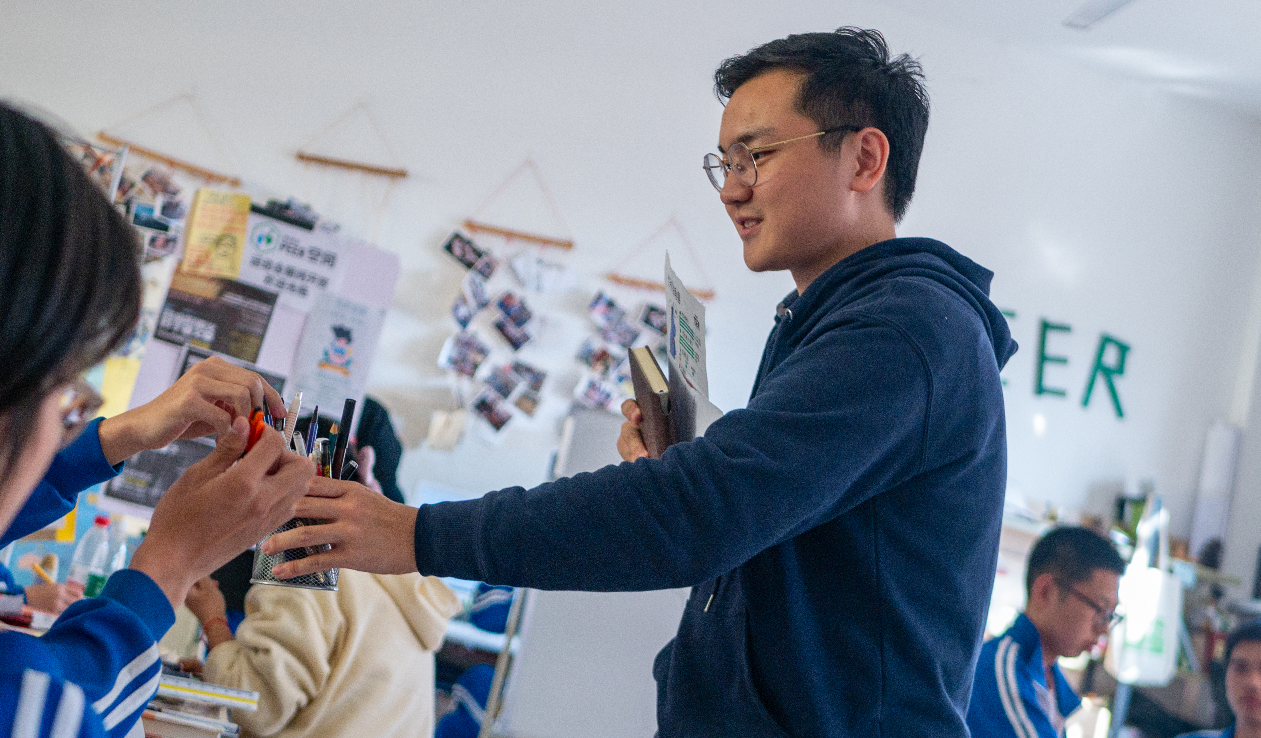 Shi hands out writing utensils to students working at tables in PEER space