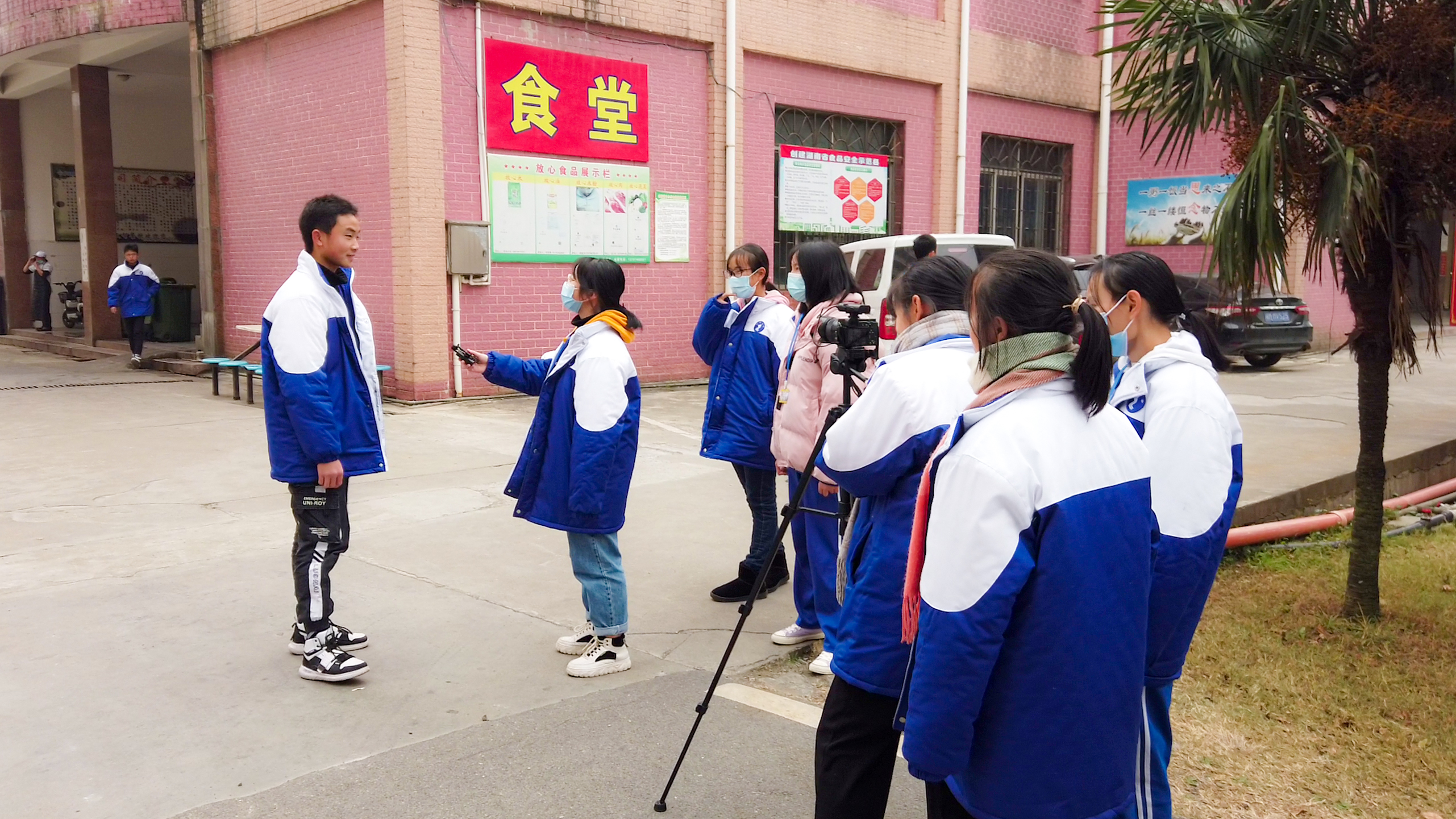 Uniformed students with camera and recorder interview classmate in front of school cafeteria