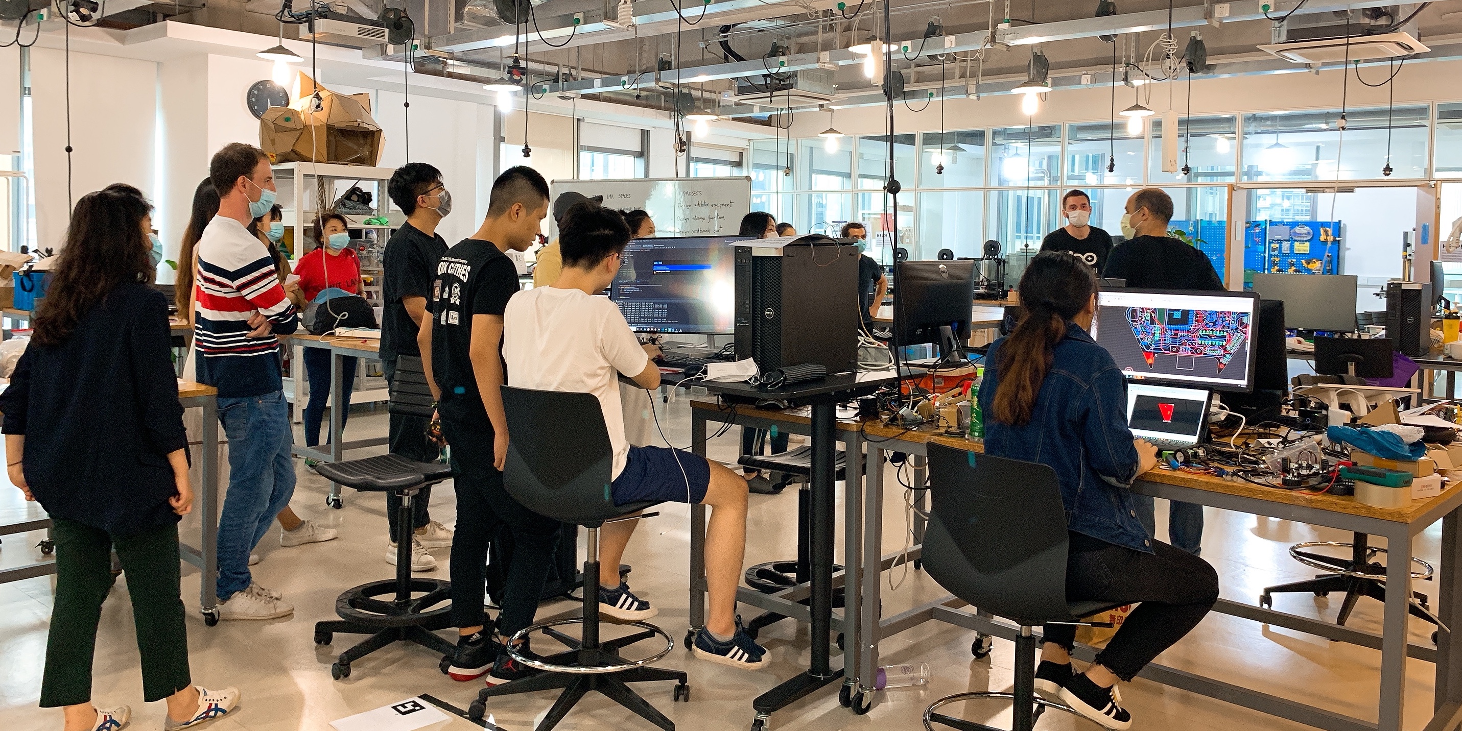 Students code and design on computer screens while professor leads others on tour