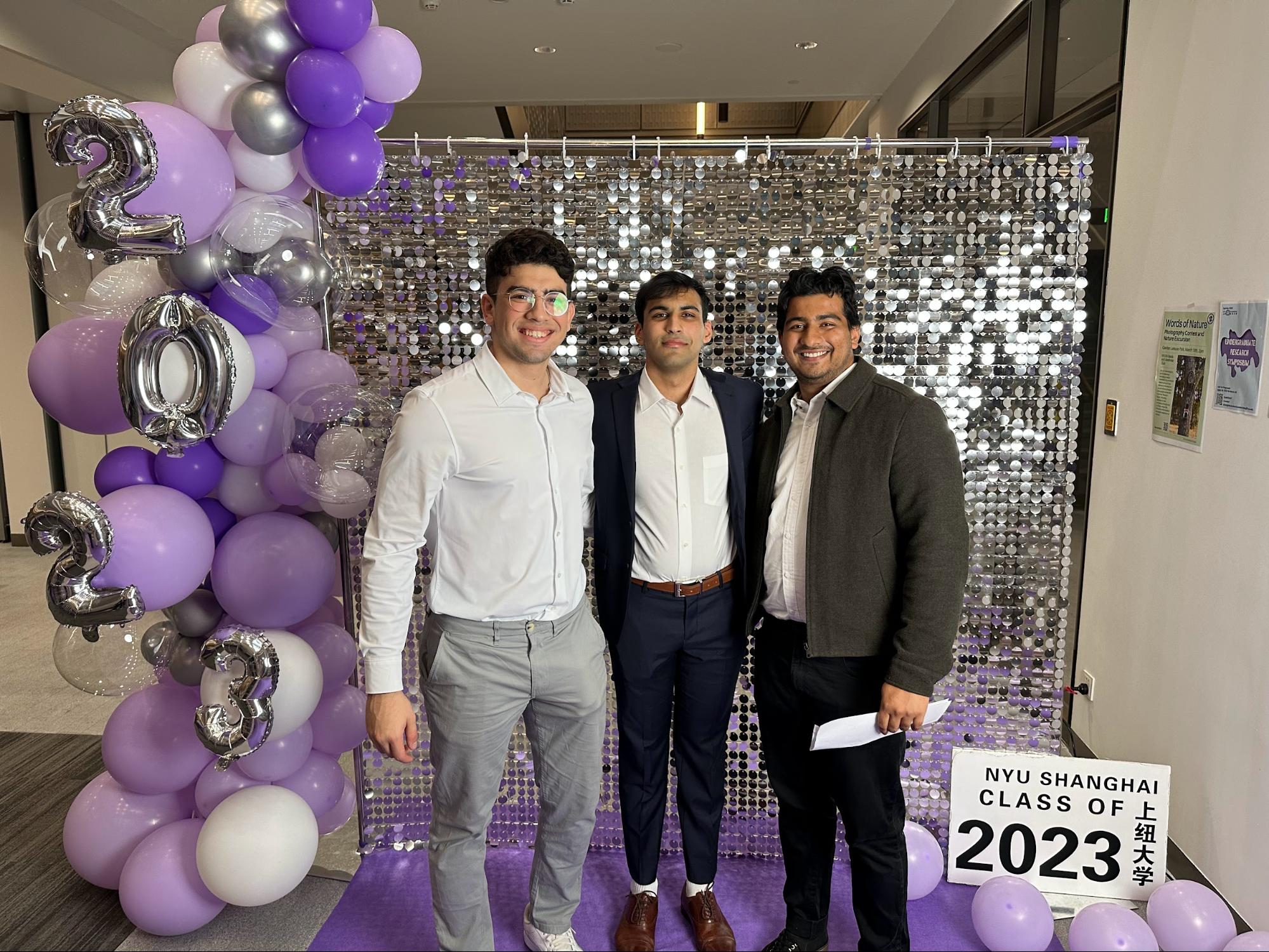 Three friends in formal attire in front of a sequined photo-booth backdrop