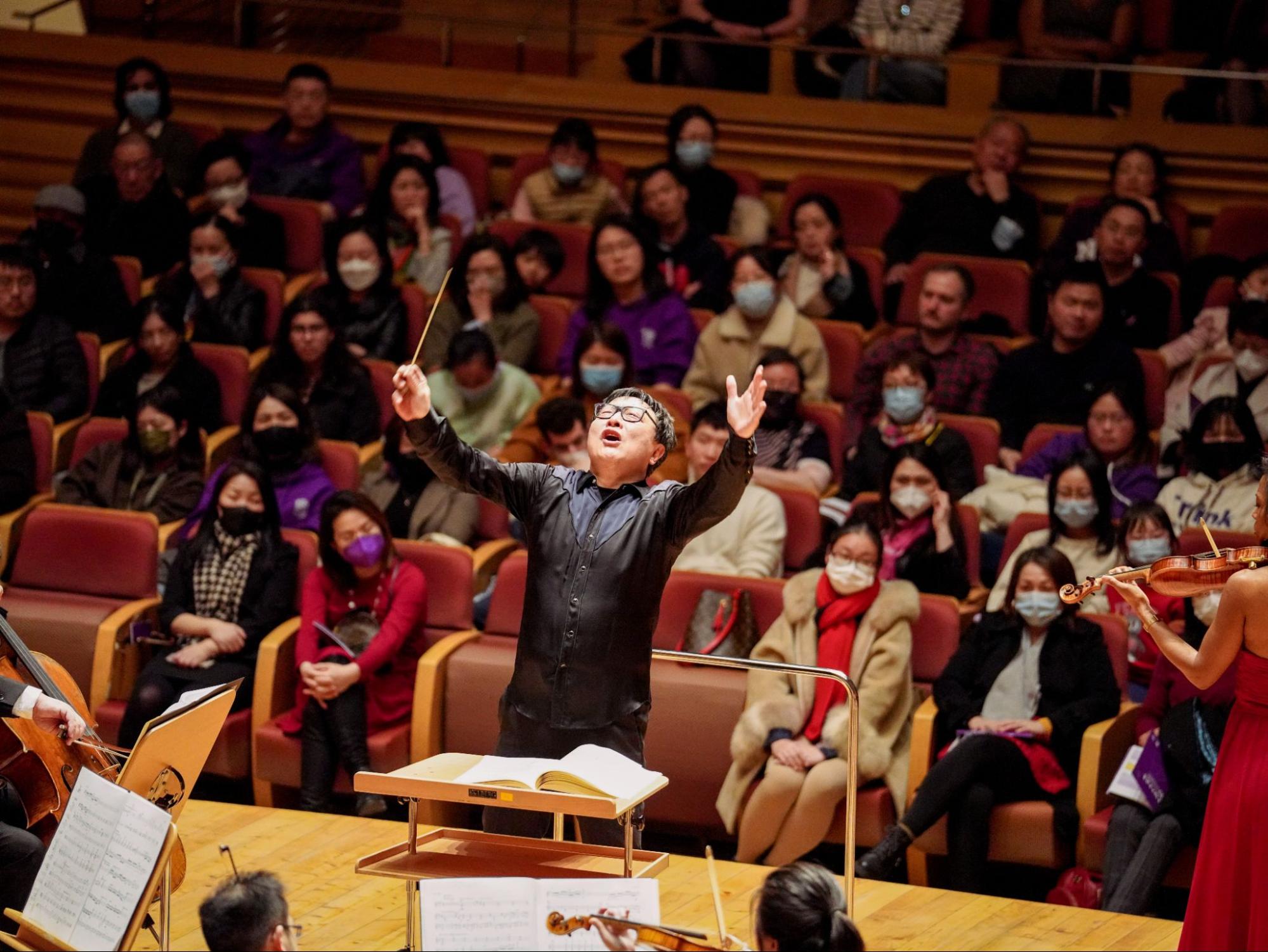 Counductor Bright Sheng with his arms in the air while conducting