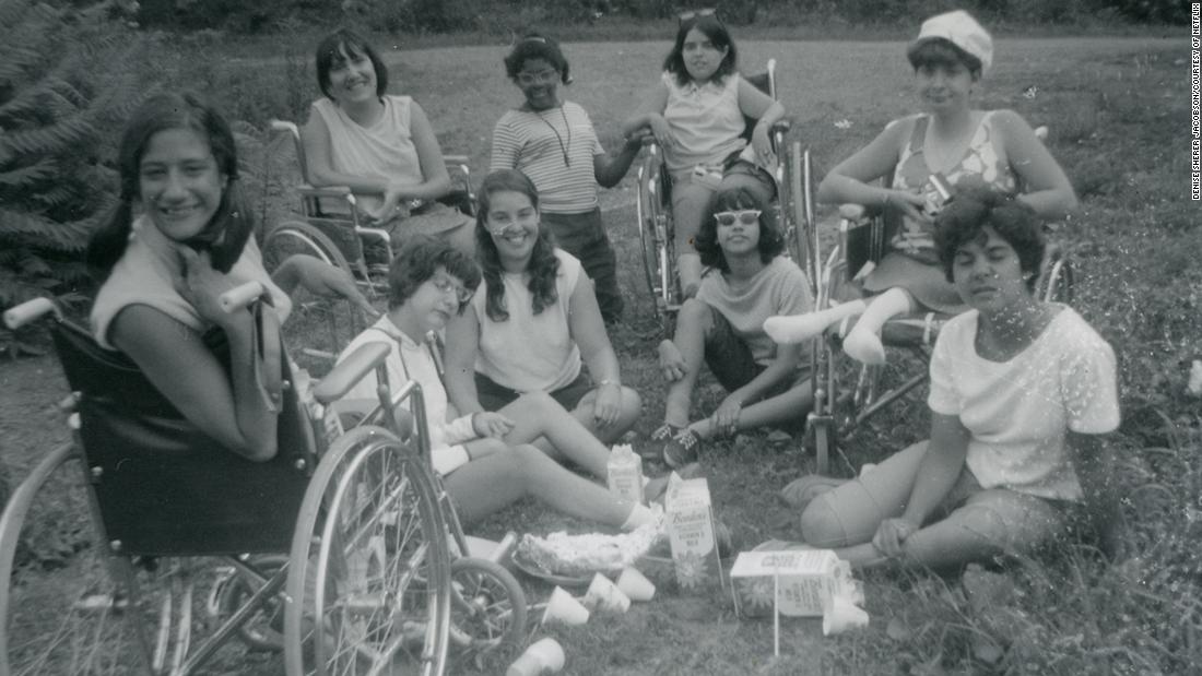 a black and white photo shows several disabled people gathering in a circle outside on a lawn