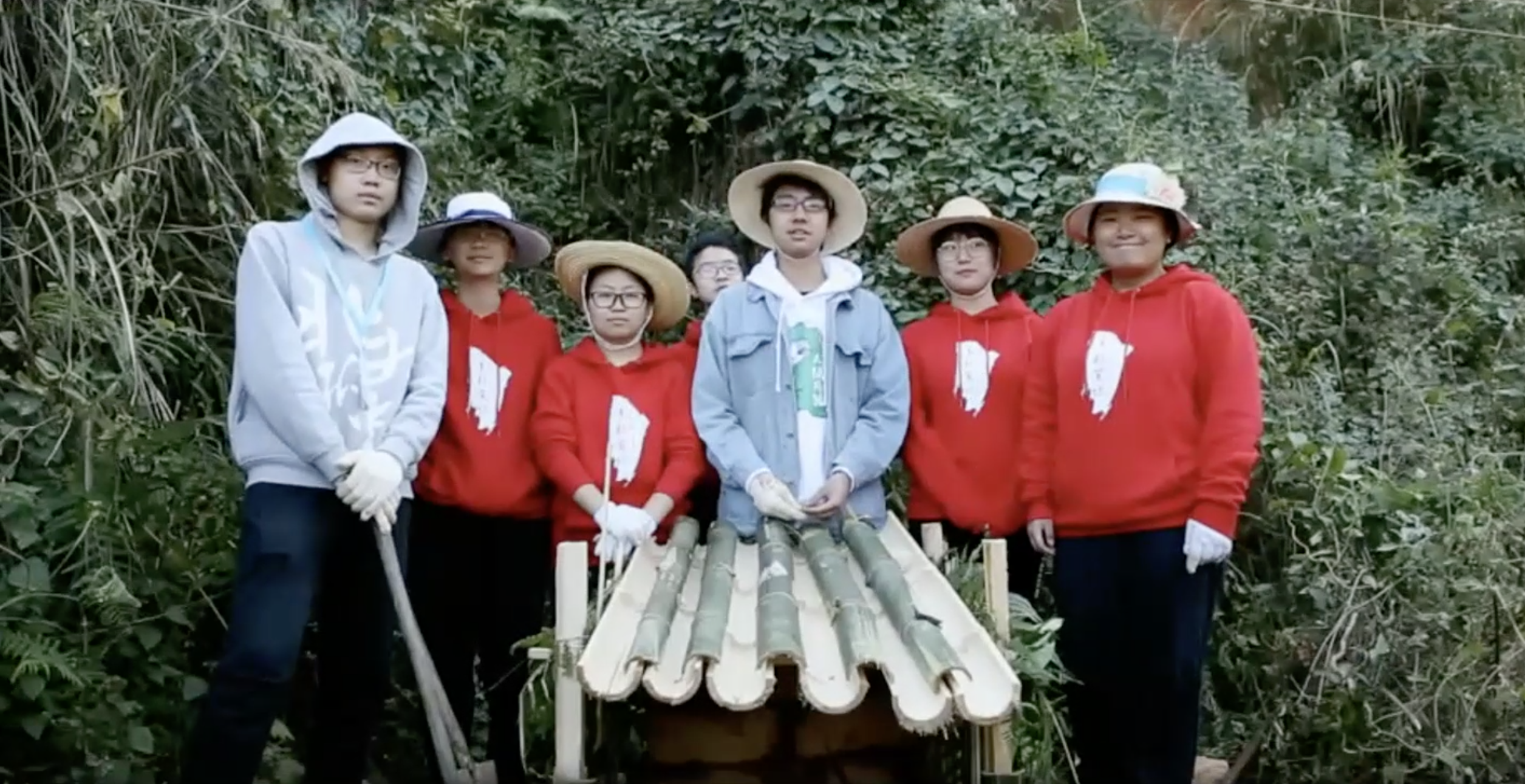 Students pose in forest with roof section handmade from fresh bamboo