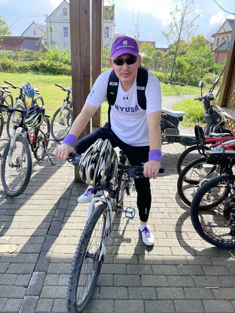 Ding posing on a bicycle and wearing a lot of NYU Shanghai purple gear