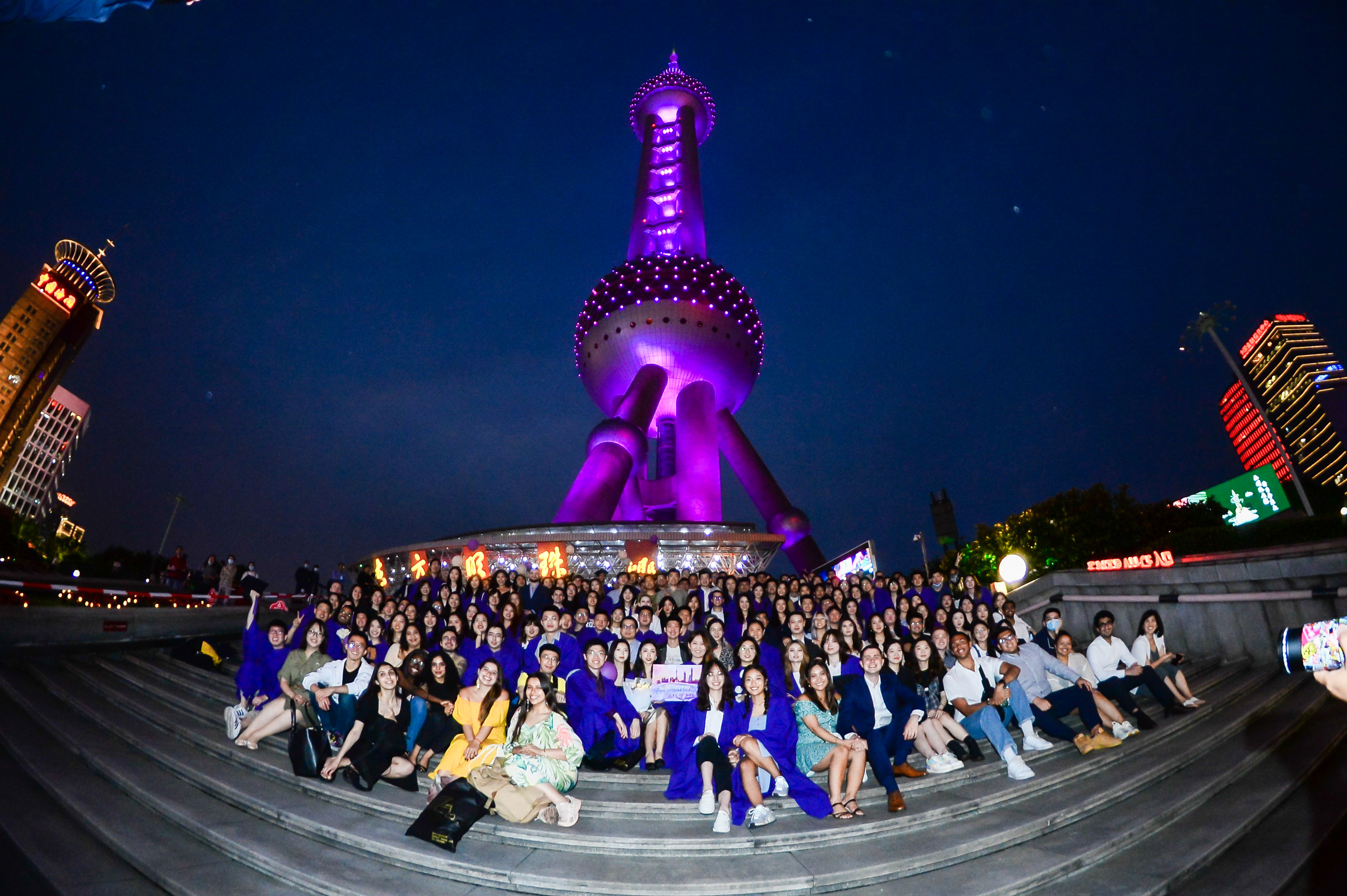 Graduates line steps at base of purple Oriental Pearl Tower