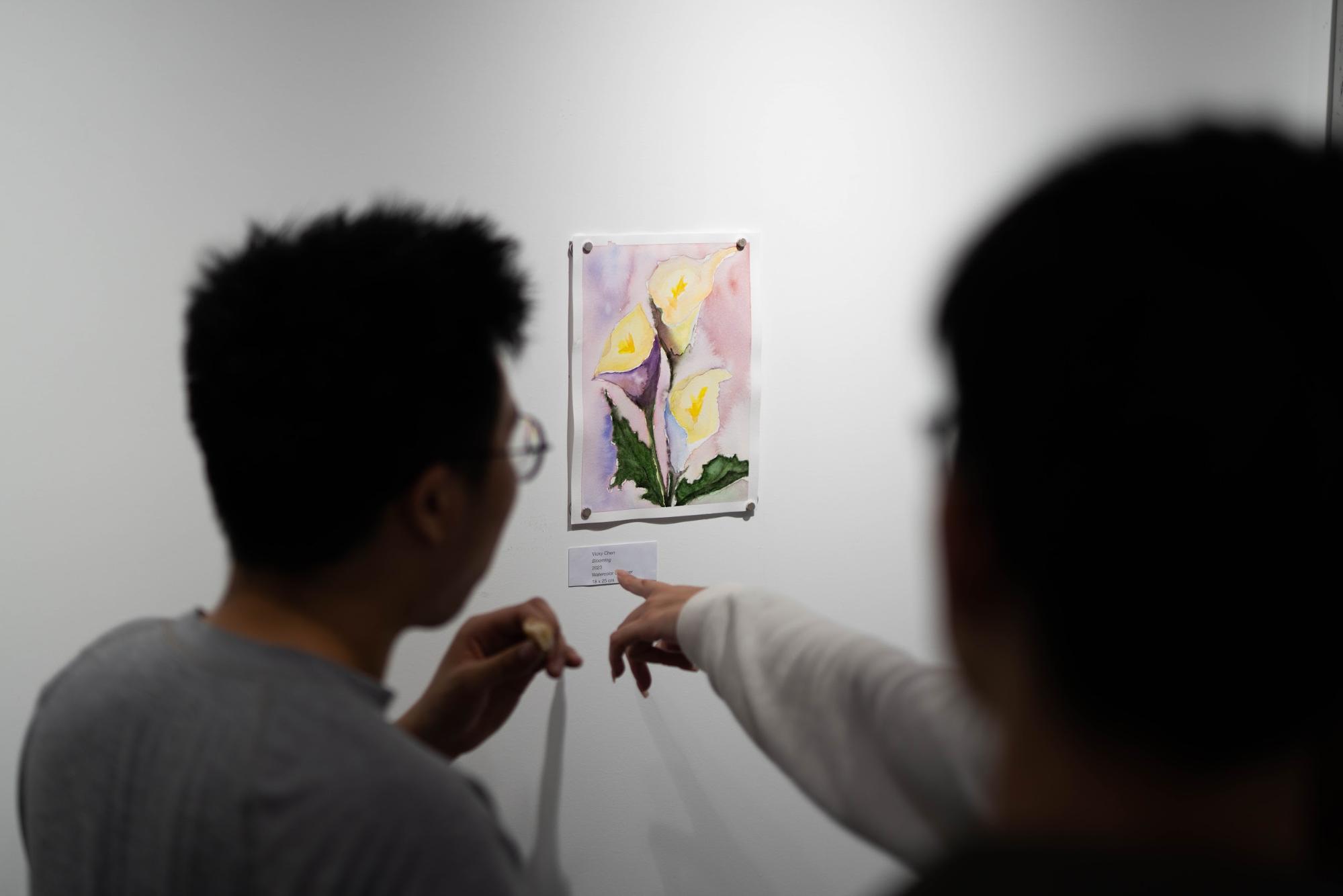 Two students in a gallery; one of them points to a painting of calla lilies
