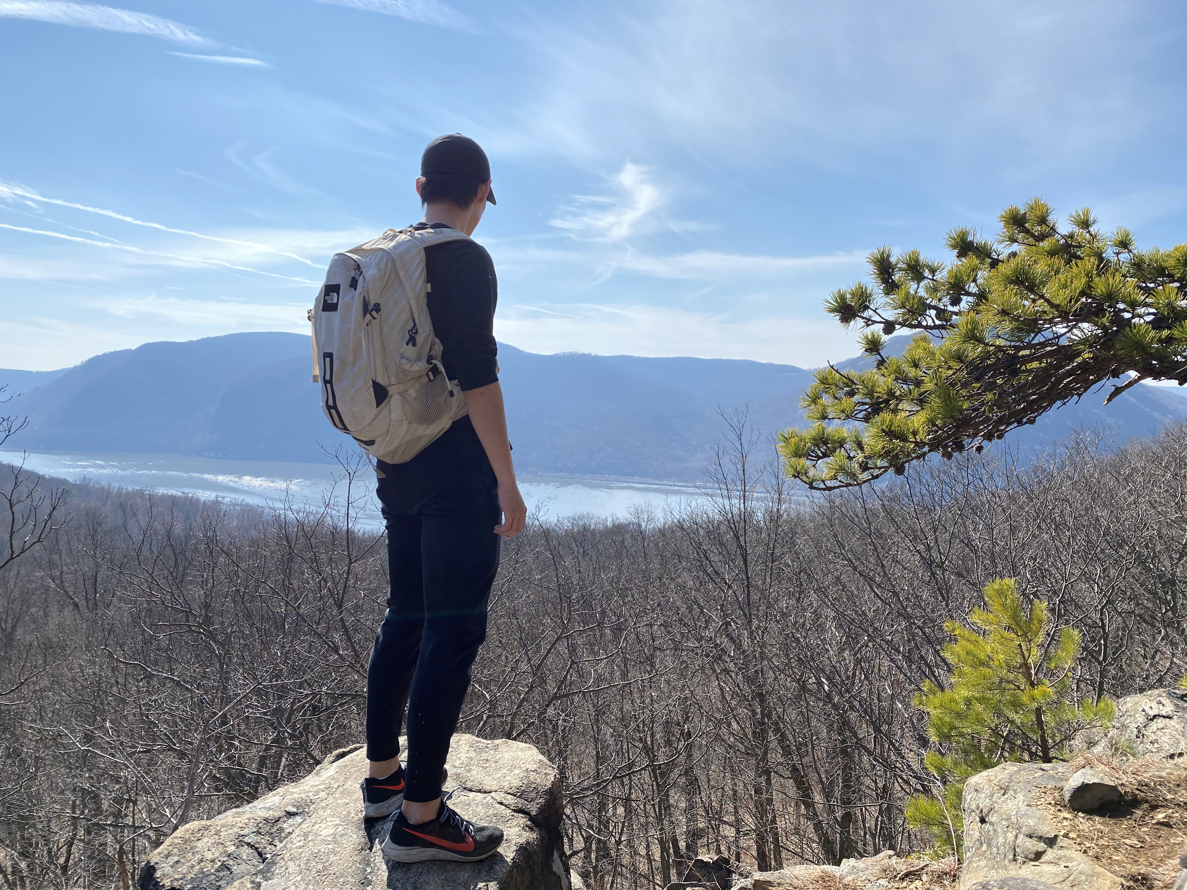 Ma stands on rocky ridge with forest of bare trees and rushing river below