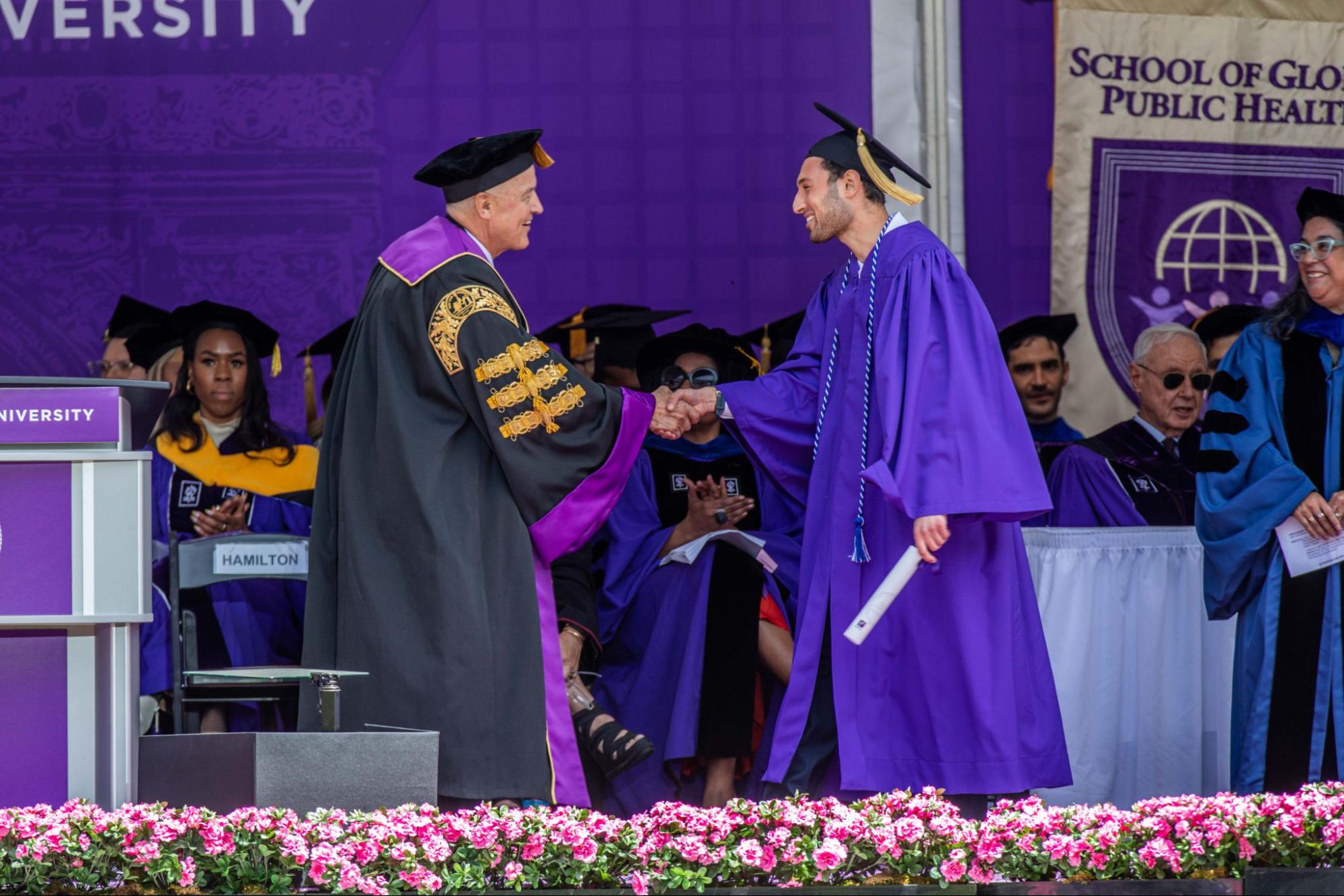 Fertig crossing the NYU graduation stage and shaking hands with the NYU President Andrew Hamilton