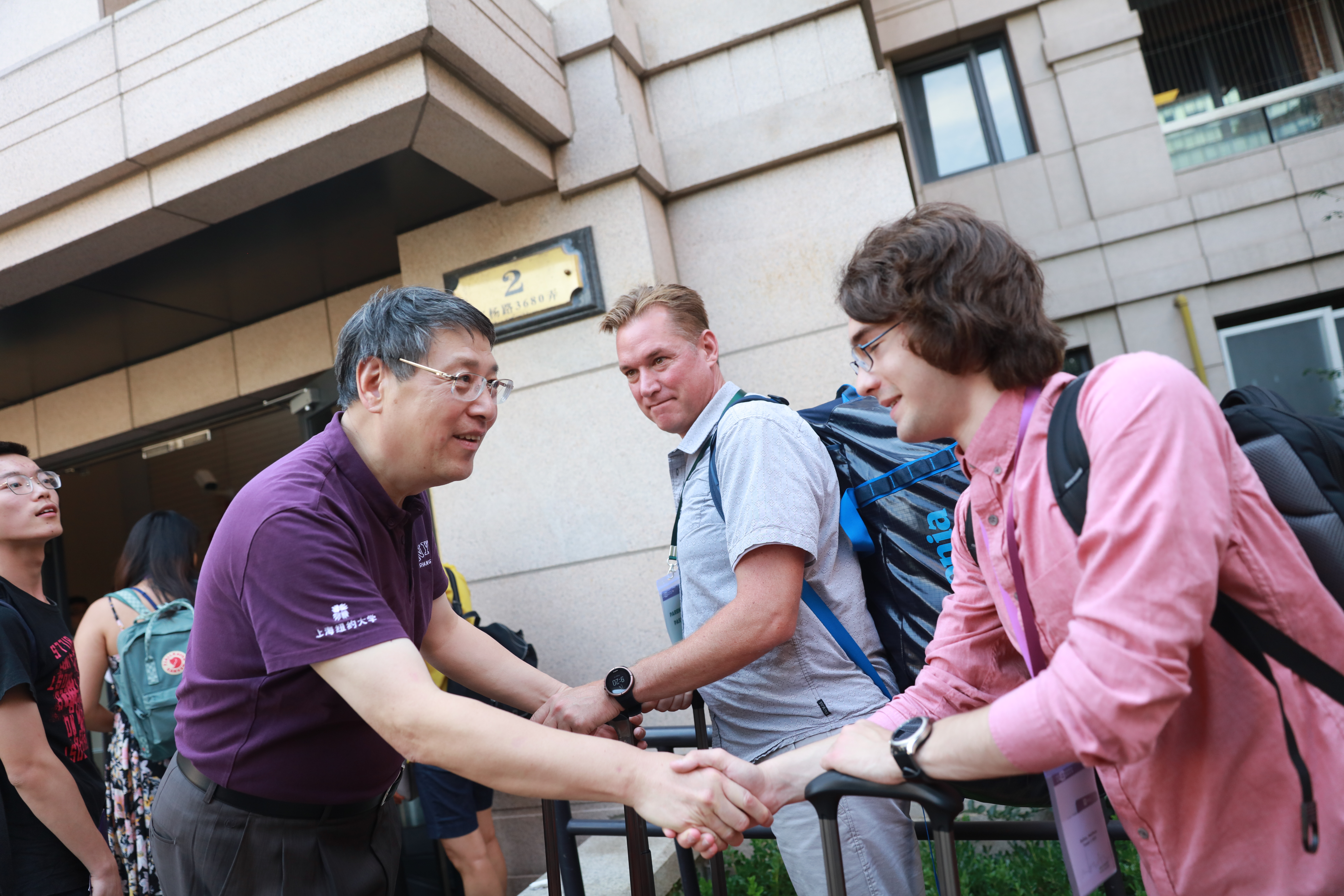 Yu shakes hands with young international student carrying luggage