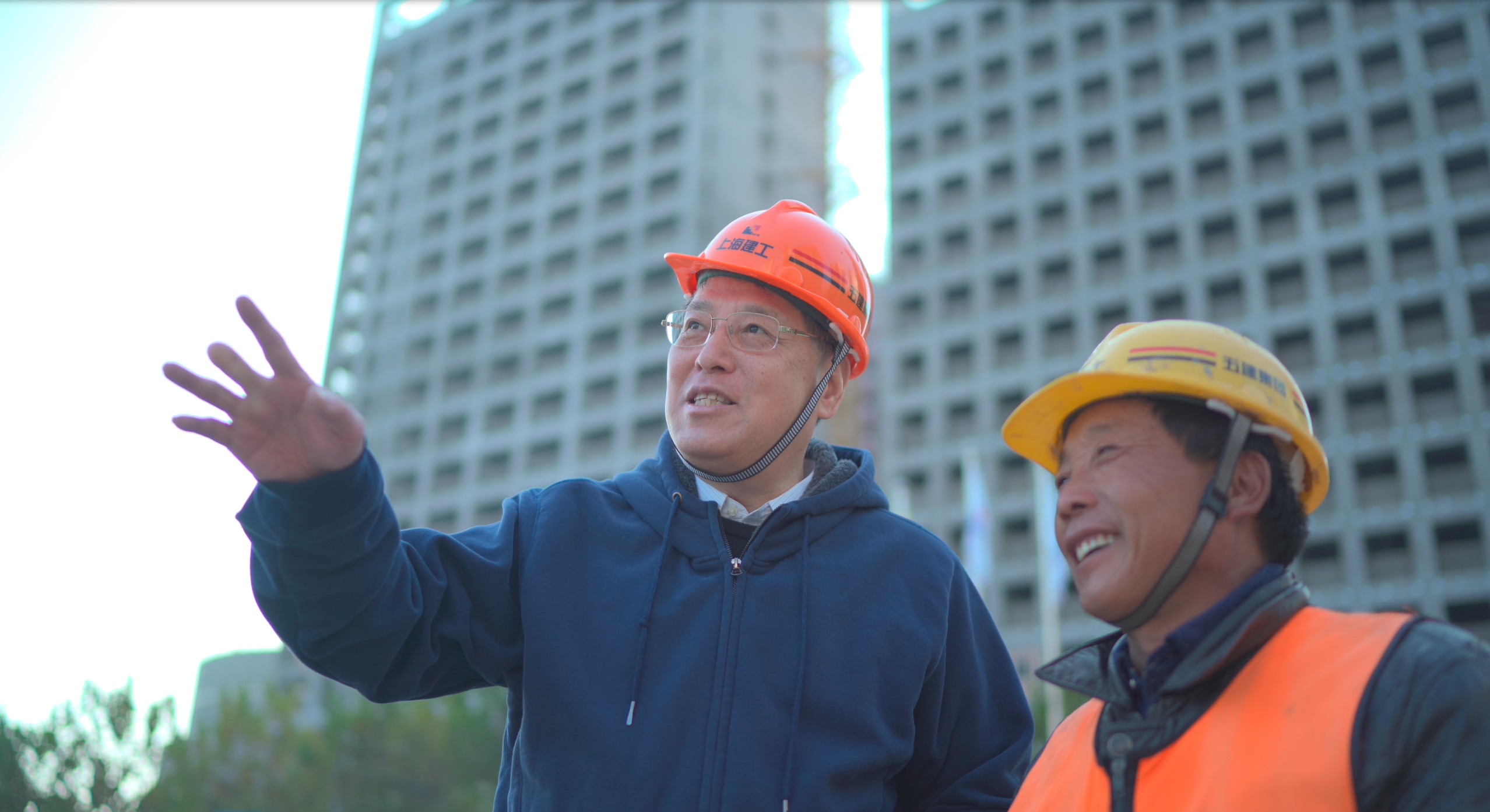 Yu, wearing hardhat, talks with construction worker at Qiantan campus building site