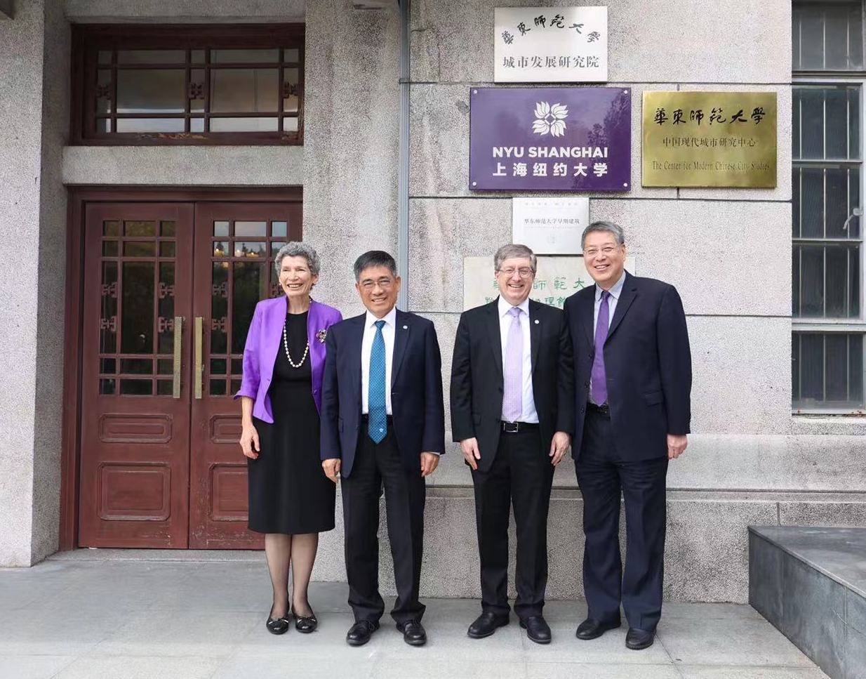 Leaders stand in front of small "NYU Shanghai" sign on building's facade