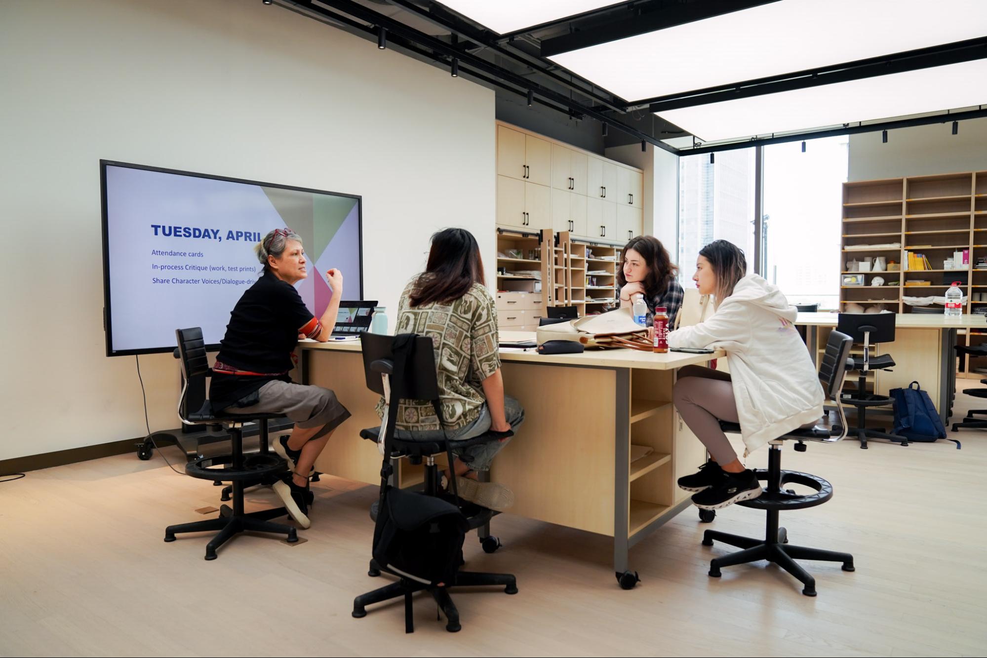 A professor and students sit around a table in an art studio