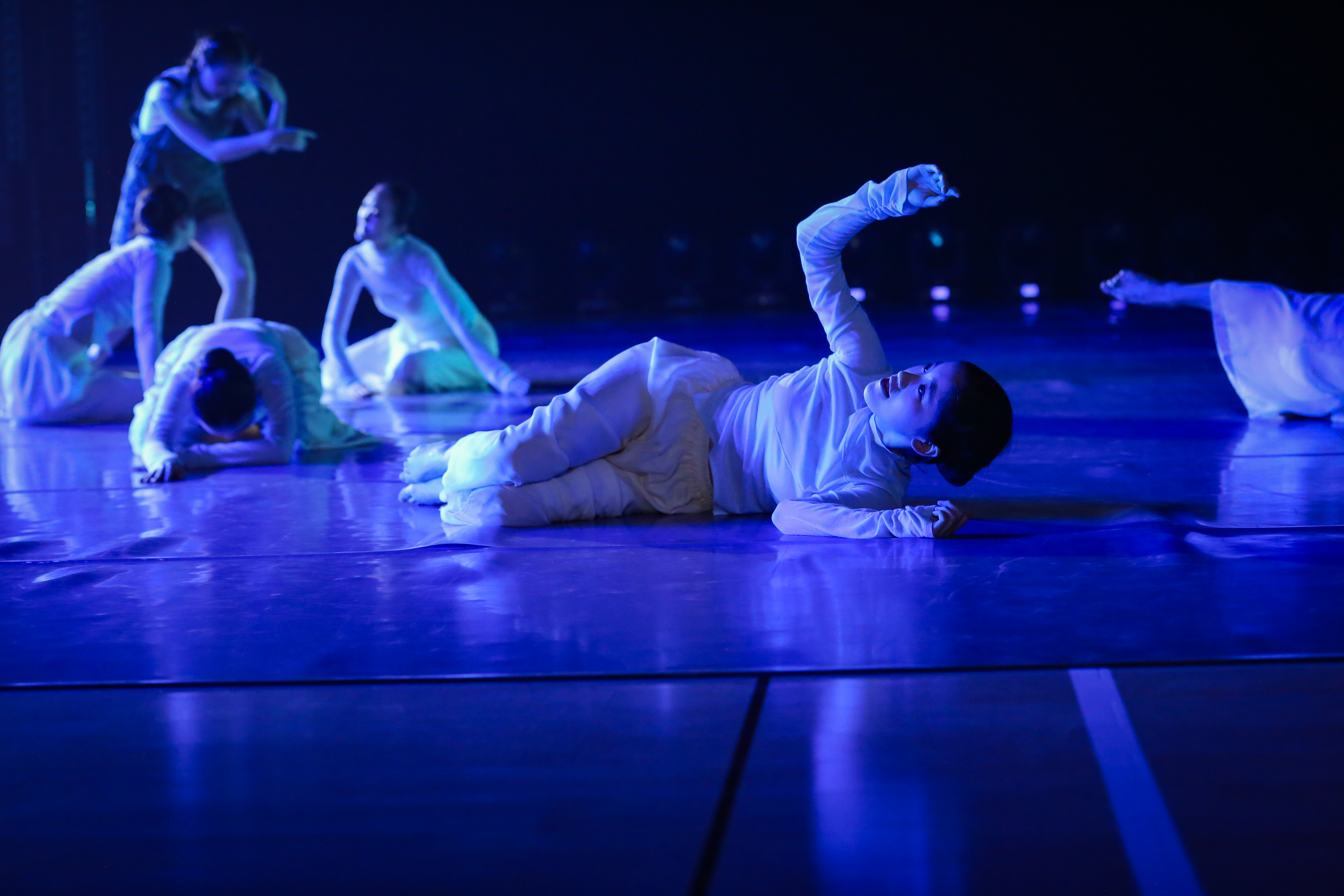 Dancer lays on floor while other dancers move in background