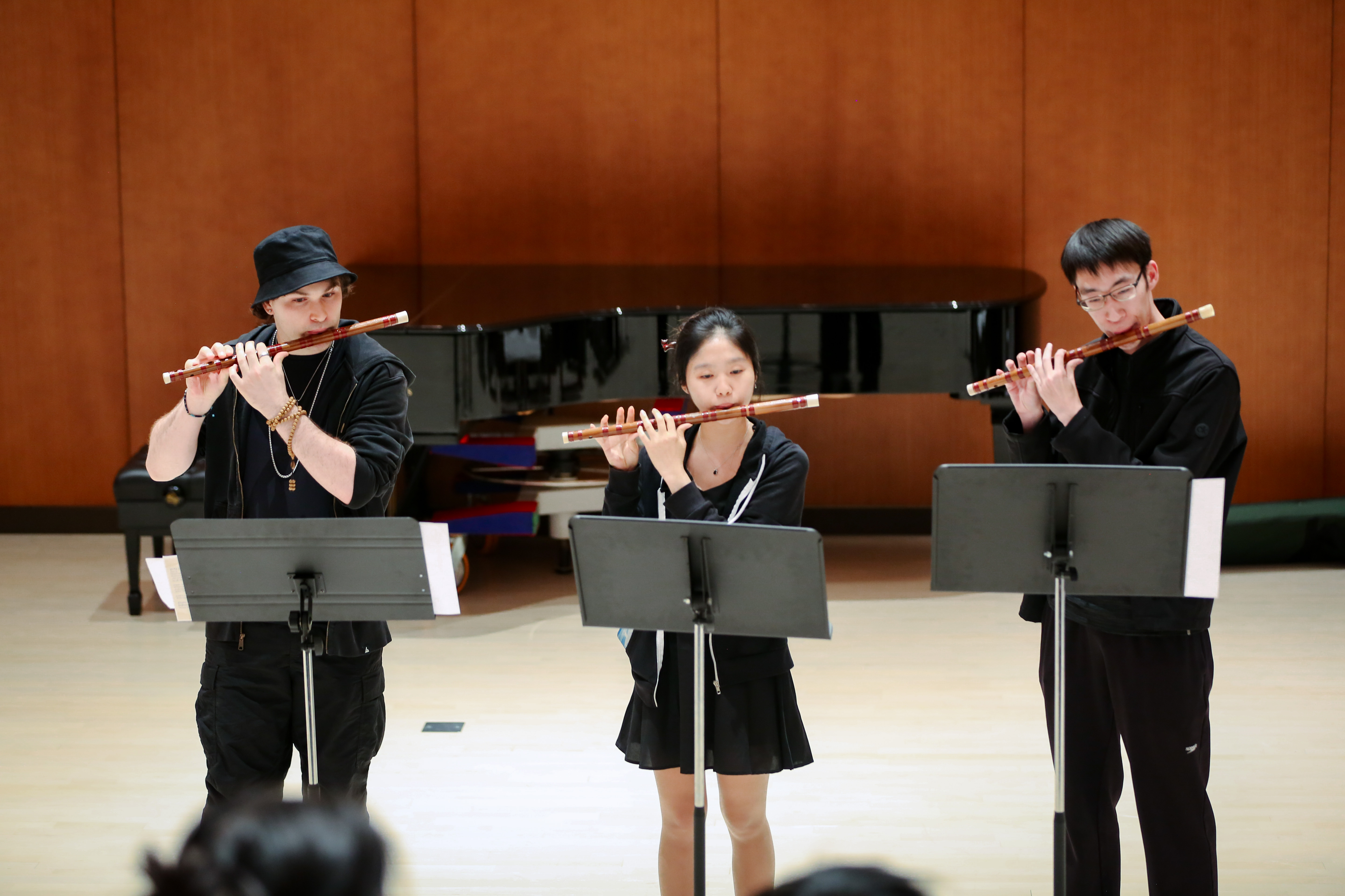 Three people wearing black play bamboo flute