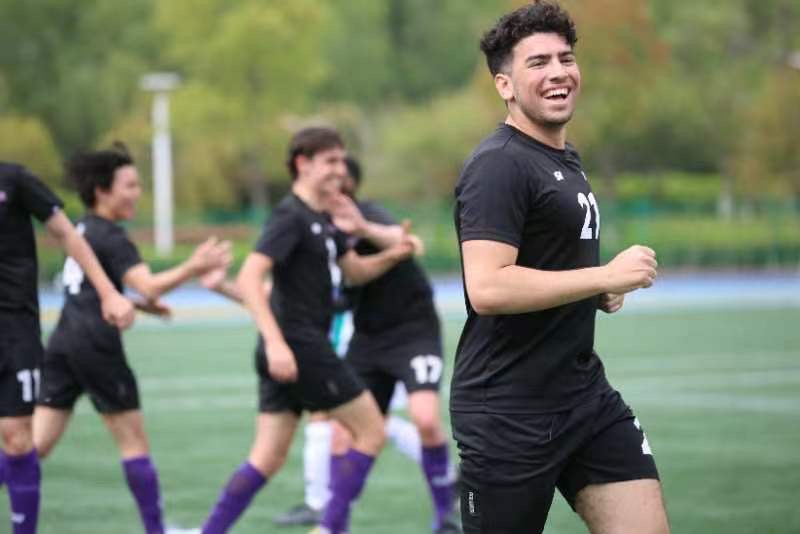 A young man in soccer uniform smiling while running on a soccer field