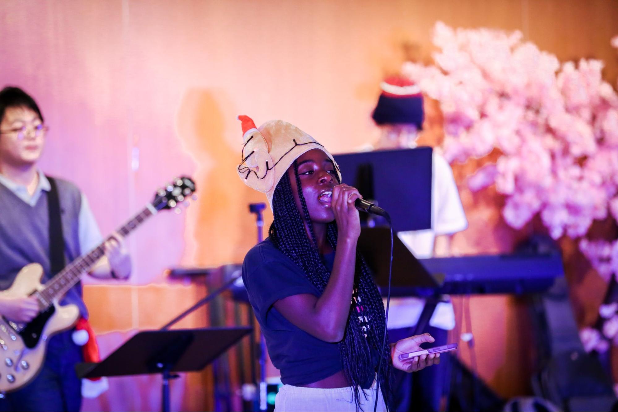 A singer wearing a turkey hat performs on stage with the backing of a band