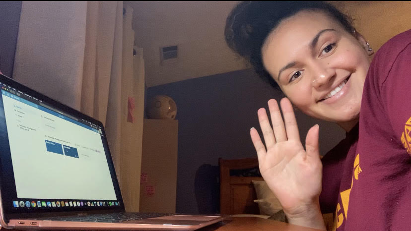 Tenielle Ellis waves at the camera while working at her laptop from home