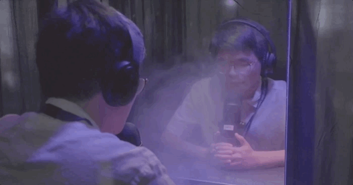 Student wearing headphones breathes into microphone in violet-illuminated booth
