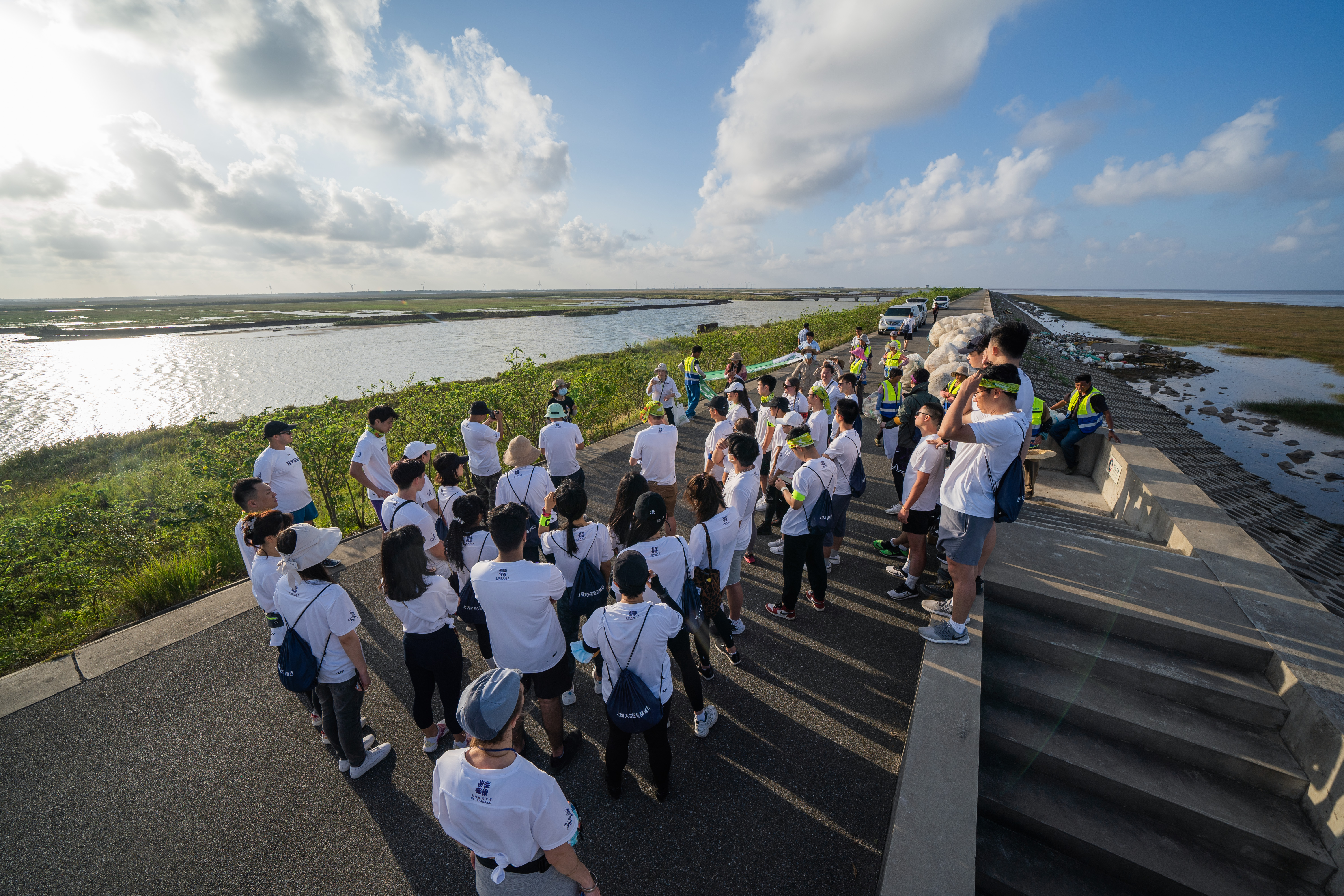 Volunteers stand on narrow paved road between wide expanses of water and marsh grass