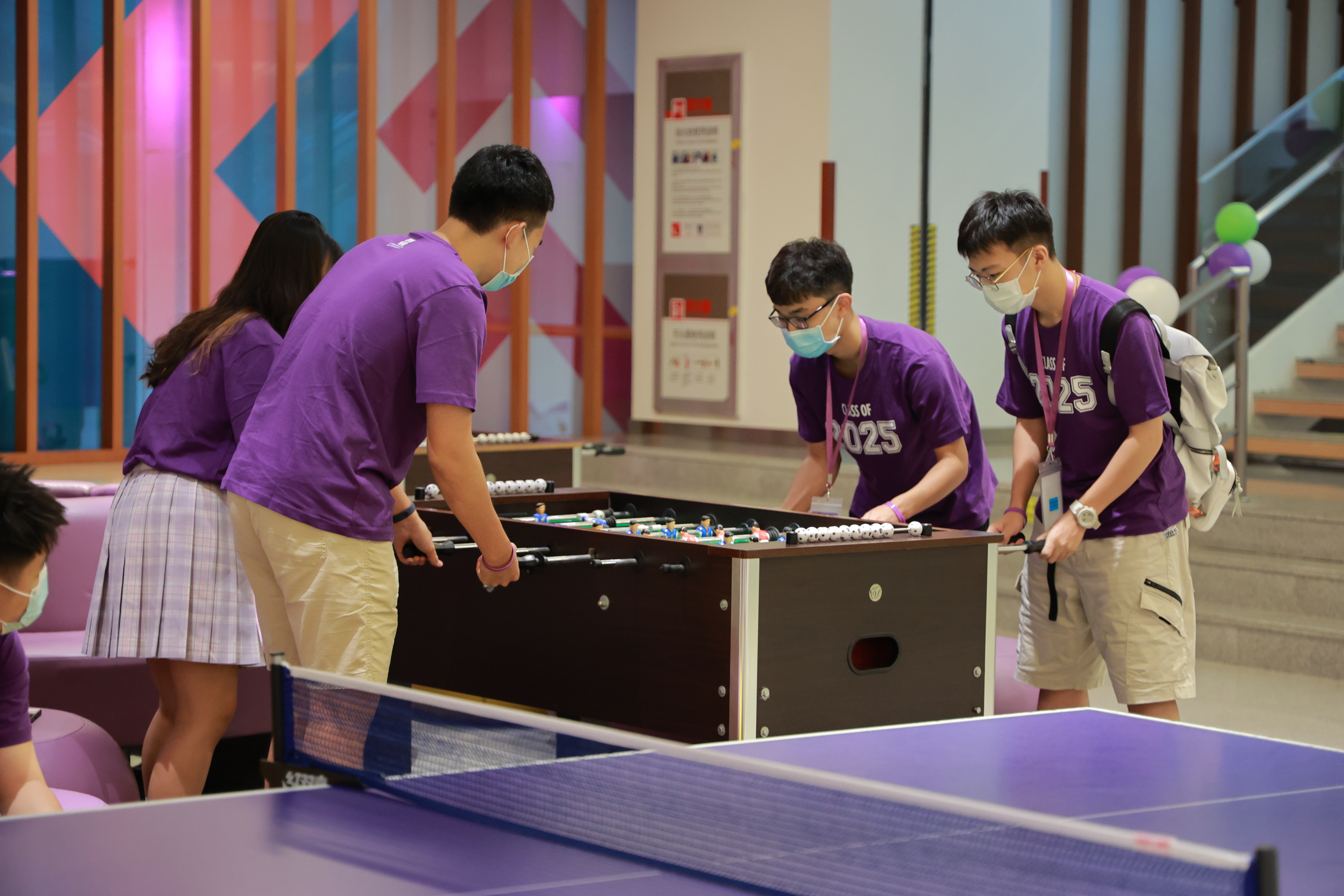 Students in purple shirts square off around a foosball table