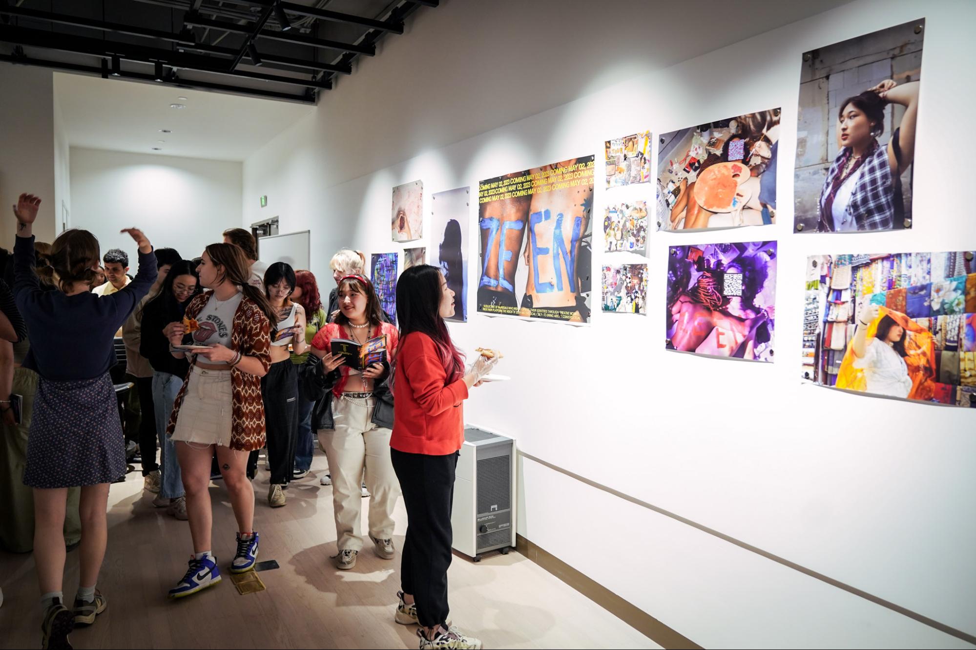 A crowd of students next to a wall covered in large art prints