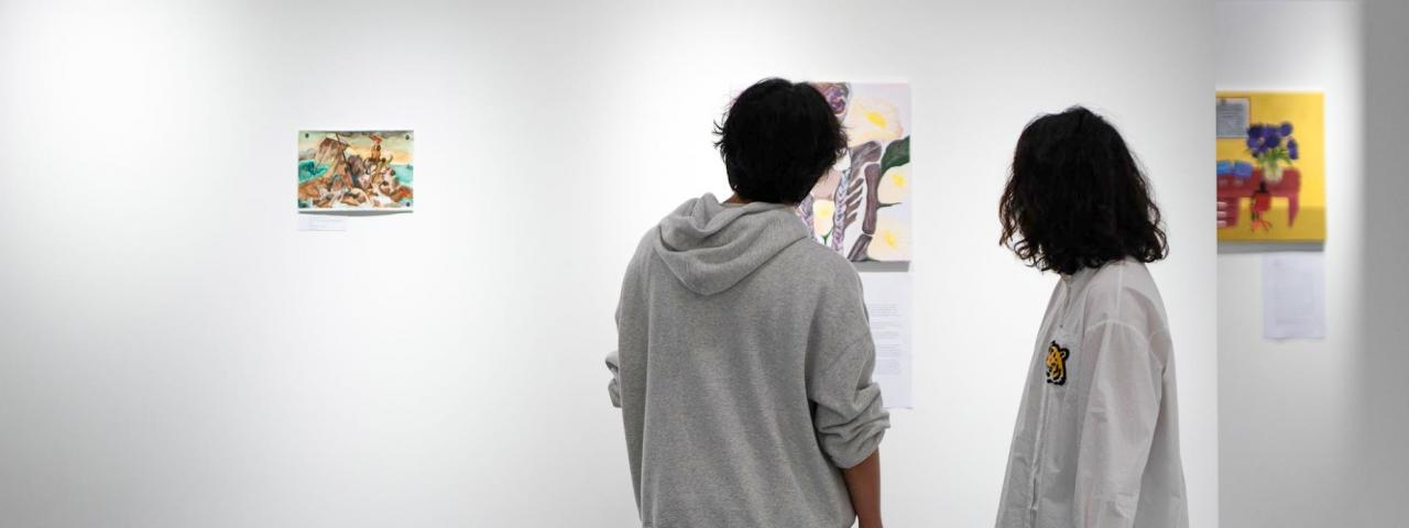 Two students admire a collection of paintings on a gallery wall