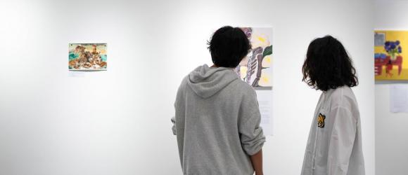 Two students admire a collection of paintings on a gallery wall