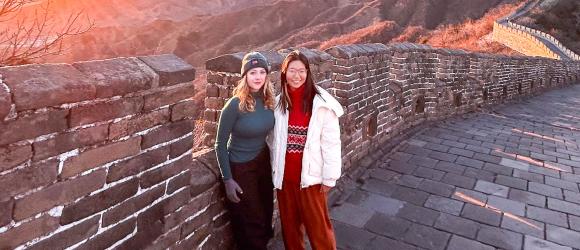 two girls stand against the Great Wall during sunset