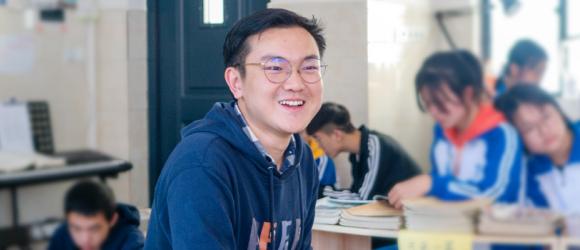 Shi laughs in classroom surrounded by students reading and writing