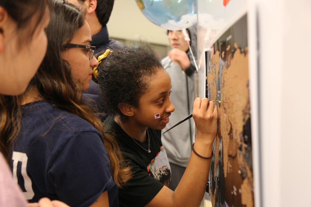 Student scratching off her hometown on a world map.