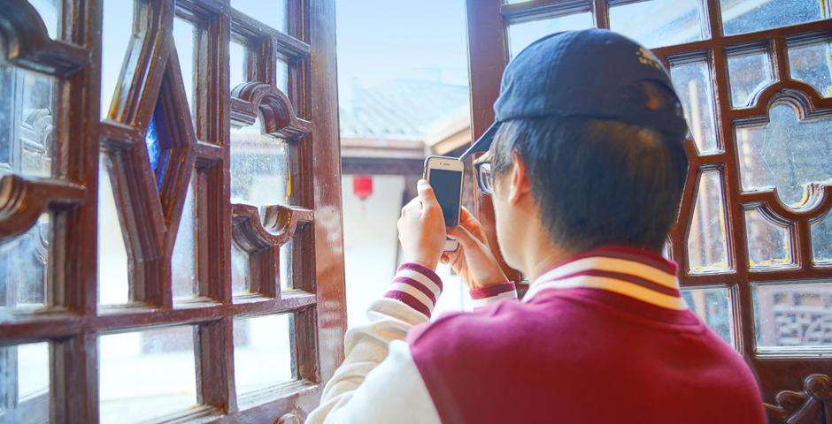 2022届互动媒体艺术与商学专业的学生卢镜合正在老宅的窗口拍照。已经退休的王慧珠是此次洋泾之旅的志愿导游，她向大家介绍道，窗户上过去安装的彩色玻璃现在已经很少见了。