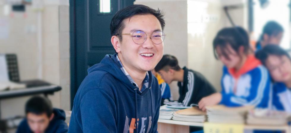 Shi laughs in classroom surrounded by students reading and writing