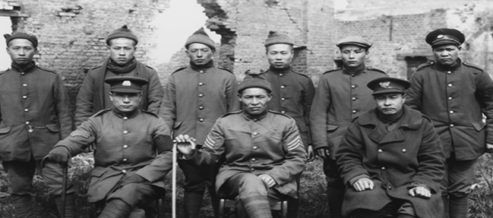 Foremen and workers in military uniform pose in front of shelled-out building