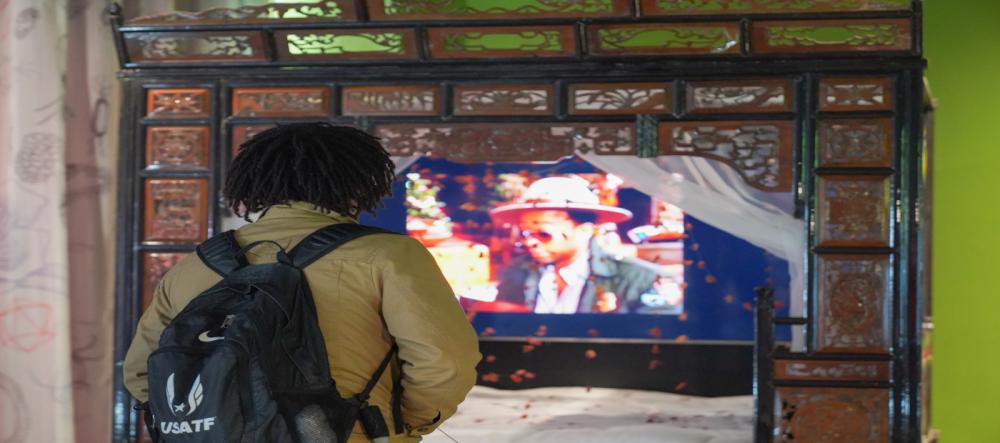 Student stands in front of Chinese traditional carved bed overlaid with video