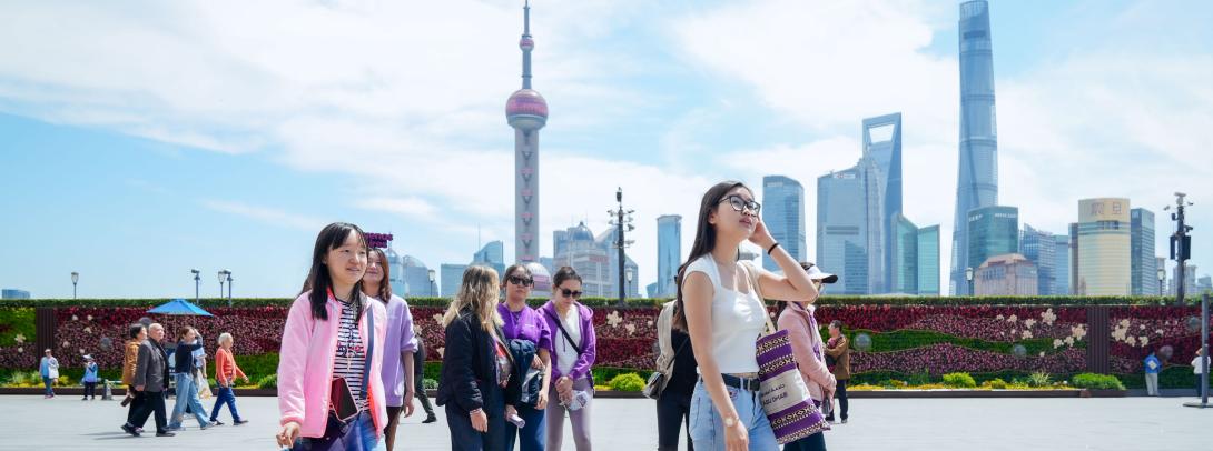 a group of students dressed in violet NYU Shanghai apparel walking on a tour of the Bund, with the Shanghai skyline in the background. 