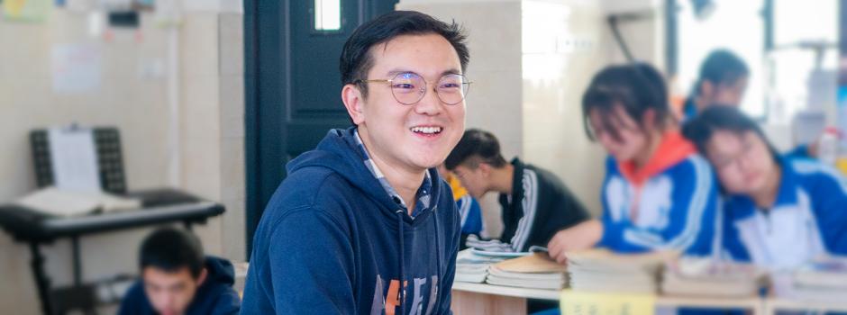 Shi laughs in classroom surrounded by students reading and writing